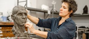 white, female presenting person working on clay sculpture of human head